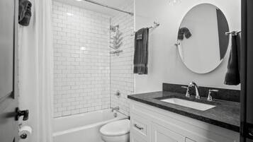 Un bany modern amb un box de dutxa de vidre, un vàter blanc, un lavabo amb taulell fosc i un mirall gran.