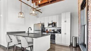A modern kitchen with white cabinetry, a central island with bar stools, and hanging pendant lights. - Huge Riverfront Loft - Walk to Conventions, Arch, Stadiums & Casino (St. Louis)