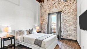 A bedroom with a white bed, a brick wall, and a window with curtains. - Huge Riverfront Loft - Walk to Conventions, Arch, Stadiums & Casino (St. Louis)