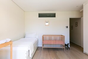 Een kamer met een bed, een babybedje, een houten bank en een kleine tafel.