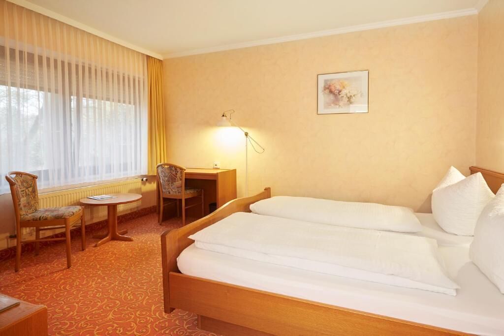 A hotel room with two beds, a desk, a chair, and a lamp.