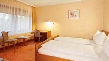 A hotel room with two beds, a desk, a chair, and a lamp.