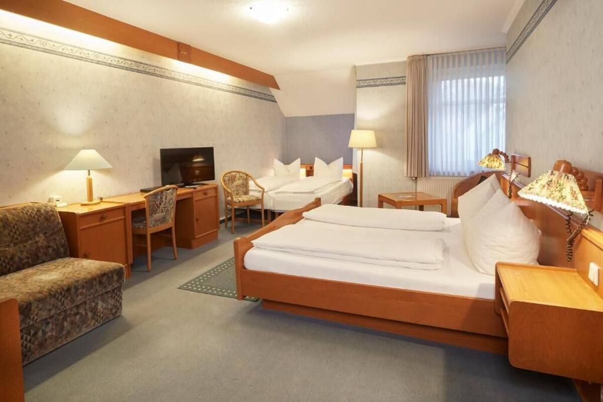 A hotel room with a bed, a desk, a chair, a television, and a lamp.
