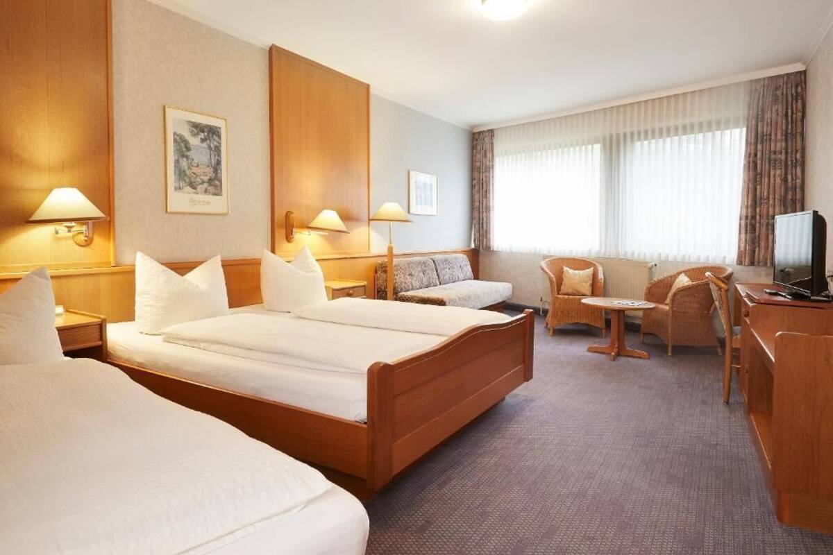 A hotel room with two beds, a sofa, a small table, and a TV.