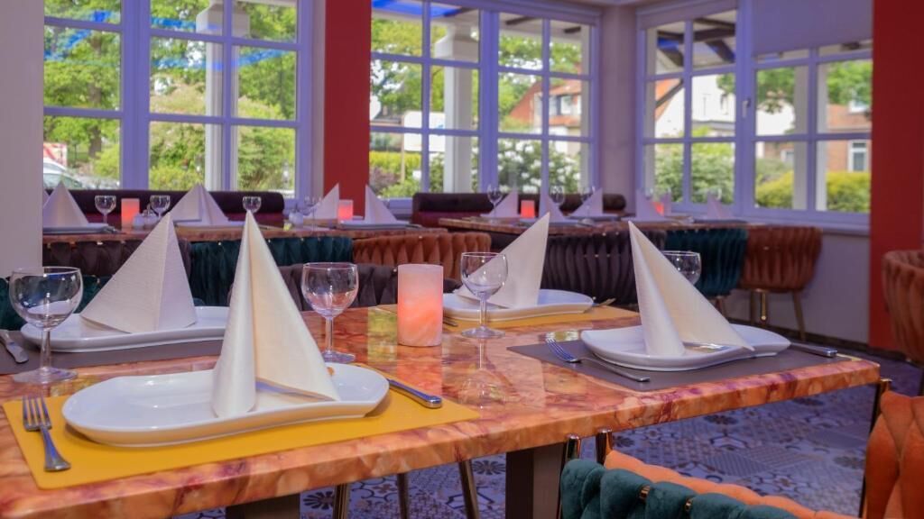 Un comedor con mesas dispuestas para dos, cada una con platos blancos, cubiertos y copas de vino.