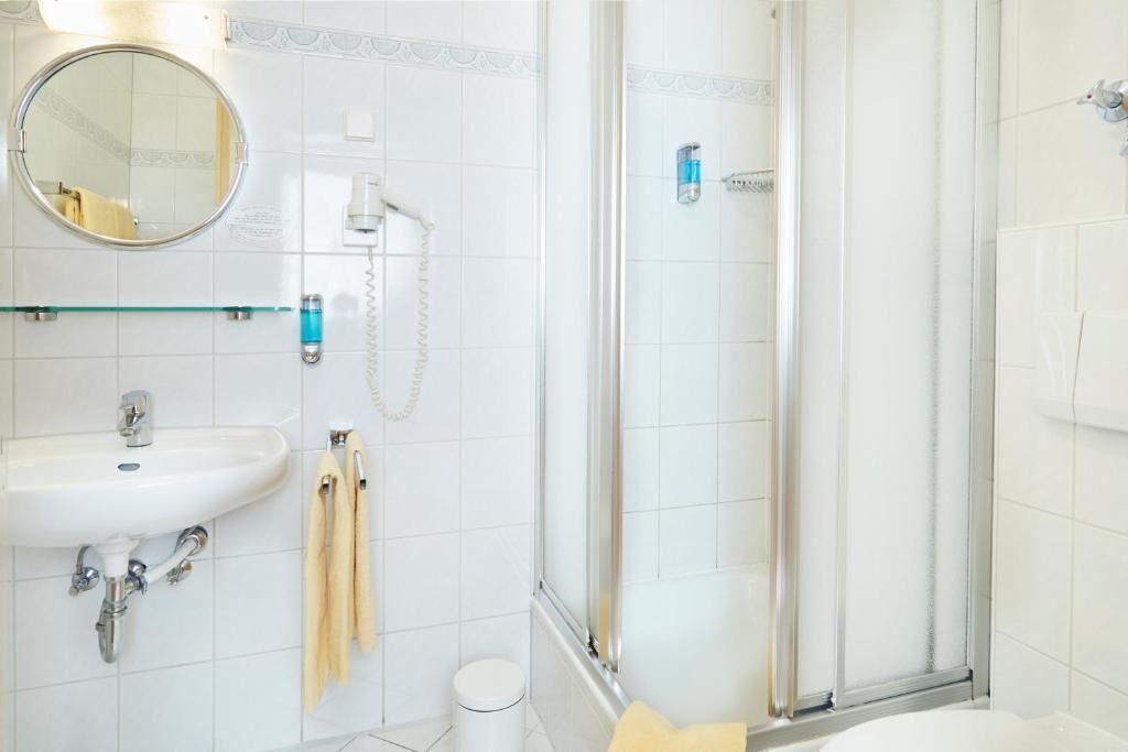 Un baño con lavamanos, espejo, toallero y cabina de ducha con mampara de vidrio.