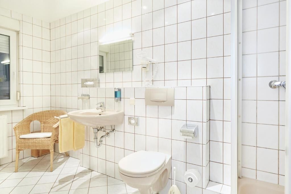 Un baño con azulejos blancos, un lavamanos, un inodoro, un espejo y una zona de ducha.