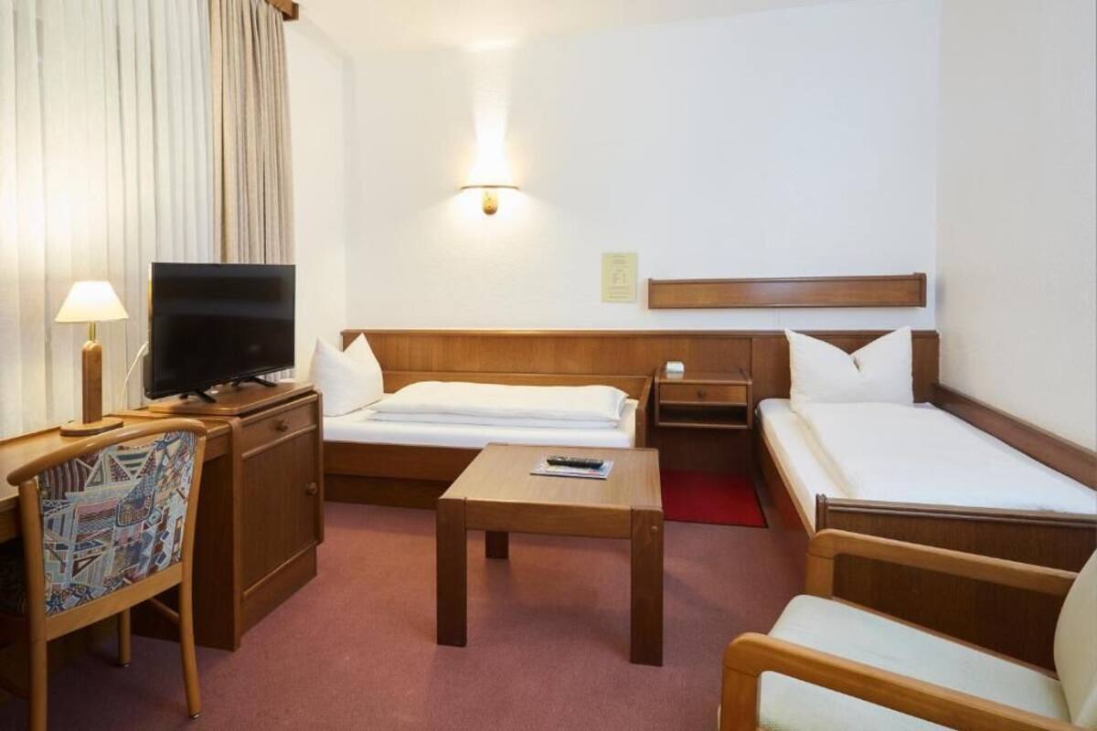 A hotel room with a bed, a desk, a chair, a television, and a bedside table.