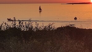 Un atardecer sobre un mar tranquilo, con un velero y una costa lejana.