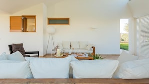 A modern living room with a sofa, coffee table, and a floor lamp. There is a window with wooden shutters and a view of greenery outside. - Affittacamere Incanto nel Verde by Wonderful Italy (Polignano a Mare)