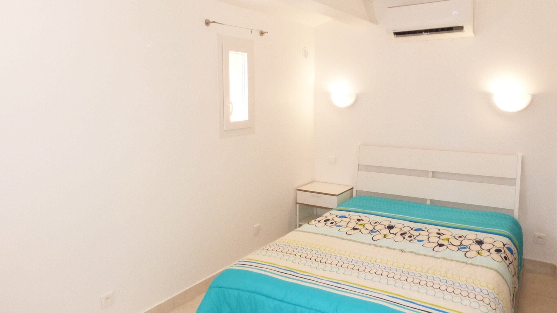 A bedroom with a bed, bedside table, and a window.