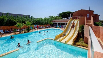 Una piscina con tobogán, sillas de descanso y un edificio con techo de tejas.