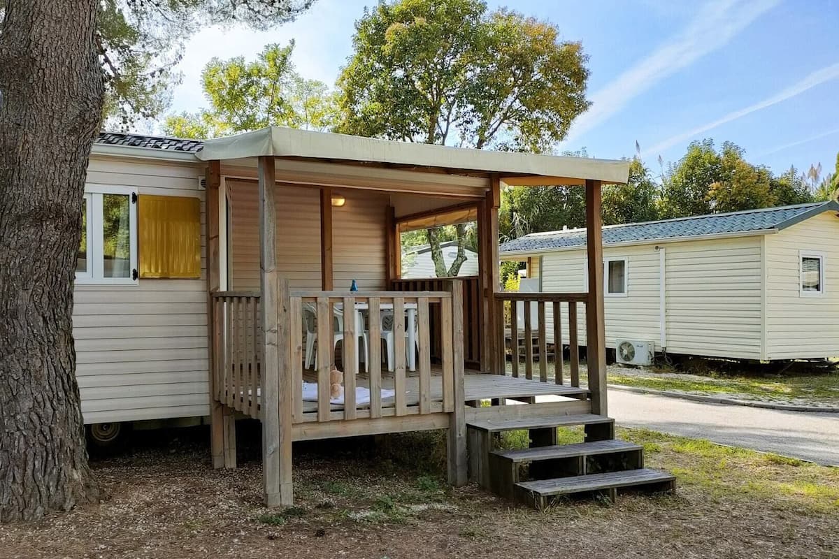 Ein Mobilheim mit einer Holzterrasse und Treppen, die zu einem überdachten Bereich führen.