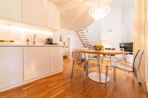 Een moderne keuken met witte kasten, een houten eettafel met stoelen en een kroonluchter.