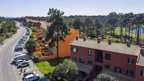 Um bairro residencial com uma fileira de carros estacionados, um edifício com telhado de cerâmica e uma vista desobstruída de uma colina arborizada ao fundo.
