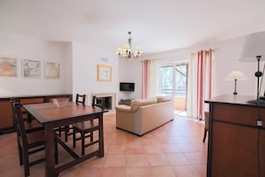 Uma sala de estar moderna com área de jantar, sofá, televisão e lustre.