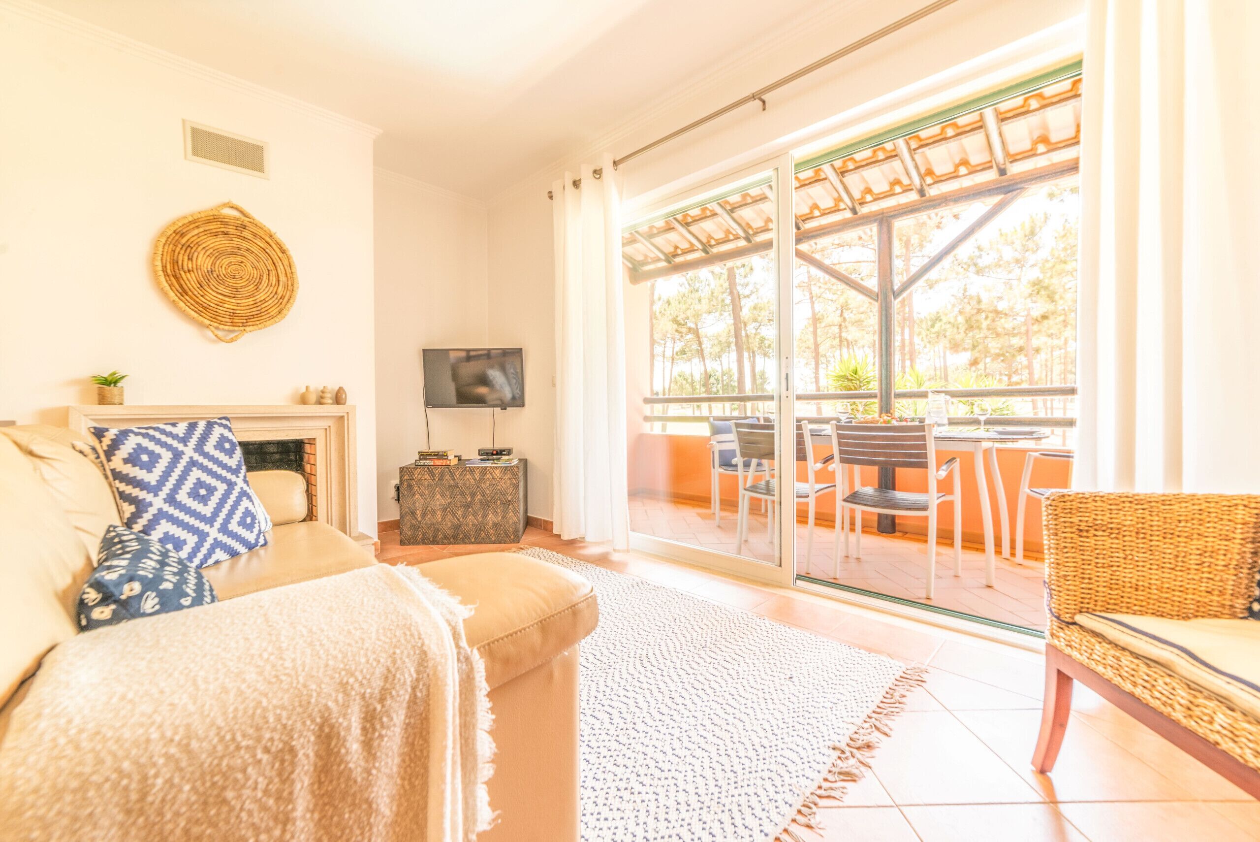 Un salon comprenant un canapé, un téléviseur, une cheminée et donnant sur une terrasse extérieure avec des chaises et une table.