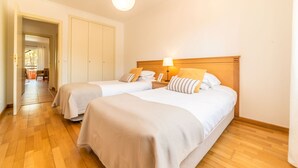A hotel room with two beds, a wooden headboard, a bedside lamp, and a view of the hallway.