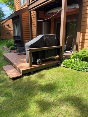 A wooden deck with a grill, outdoor chairs, and a small garden area.