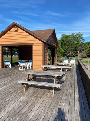 A wooden building with a covered patio area, picnic tables, and lounge chairs.