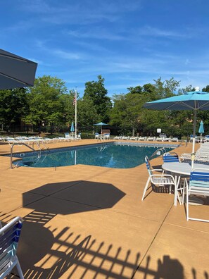 A pool area with lounge chairs and umbrellas, surrounded by a fence and trees.