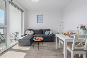 A modern living space with a sectional sofa, a dining table, and a large window. - Ursus Habicha (Warsaw)