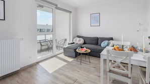 A modern living room with a sofa, a dining table with chairs, a radiator, and a sliding glass door leading to an outdoor area. - Ursus Habicha (Warsaw)