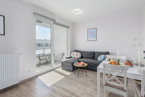 A modern living room with a sofa, a dining table with chairs, a radiator, and a sliding glass door leading to an outdoor area. - Ursus Habicha (Warsaw)