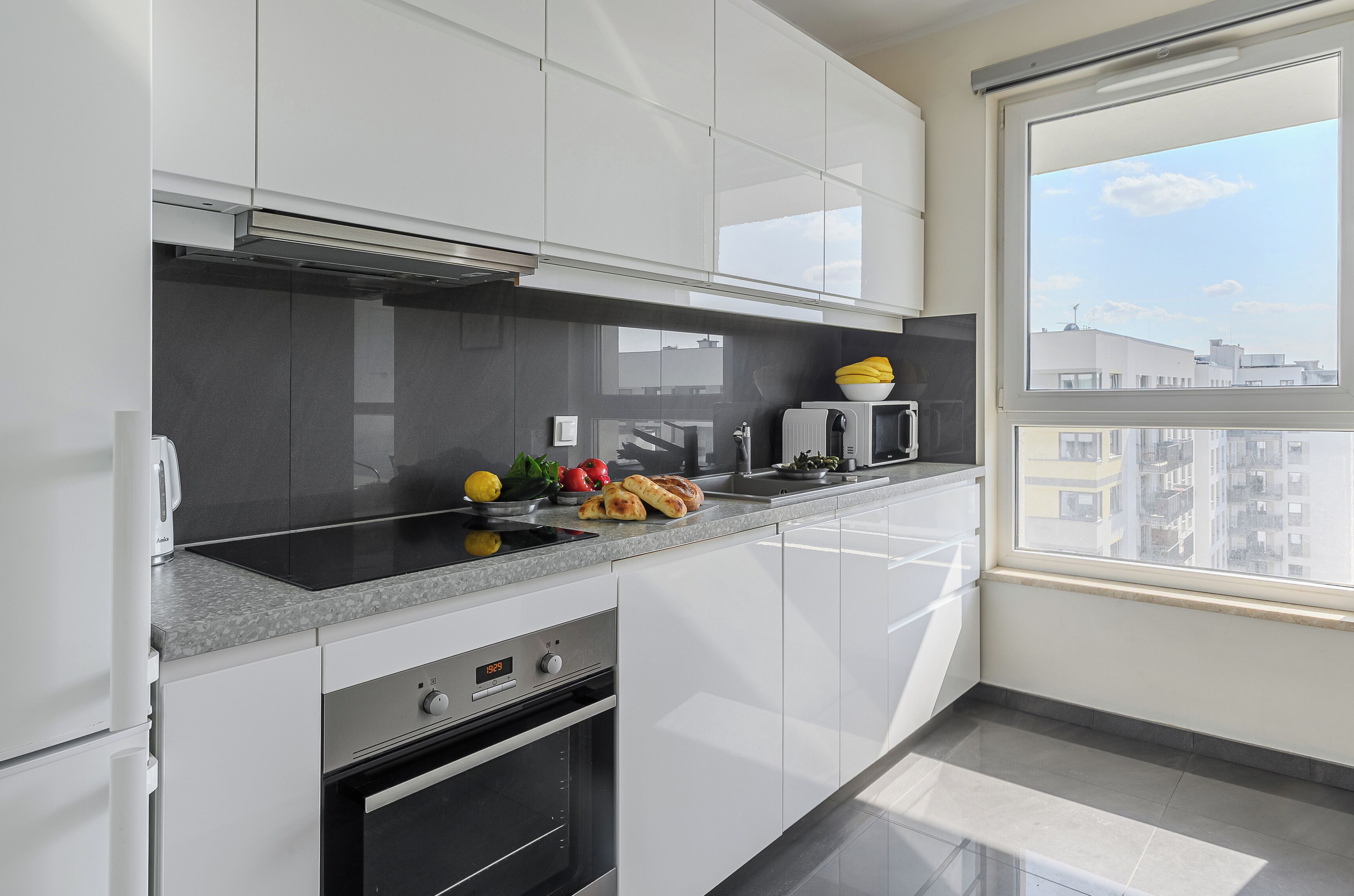 Eine moderne Küche mit weißen Schränken, einem Backofen und einem Fenster mit Blick auf die Stadt.