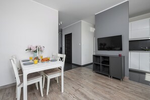 A modern kitchen with grey cabinets, a built-in TV, and a dining area with a white table and chairs. - Ursus Habicha (Warsaw)