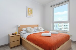 A neatly made bed with an orange blanket, a wooden headboard, and a nightstand with a plate of food and a glass of orange juice. - Ursus Habicha (Warsaw)