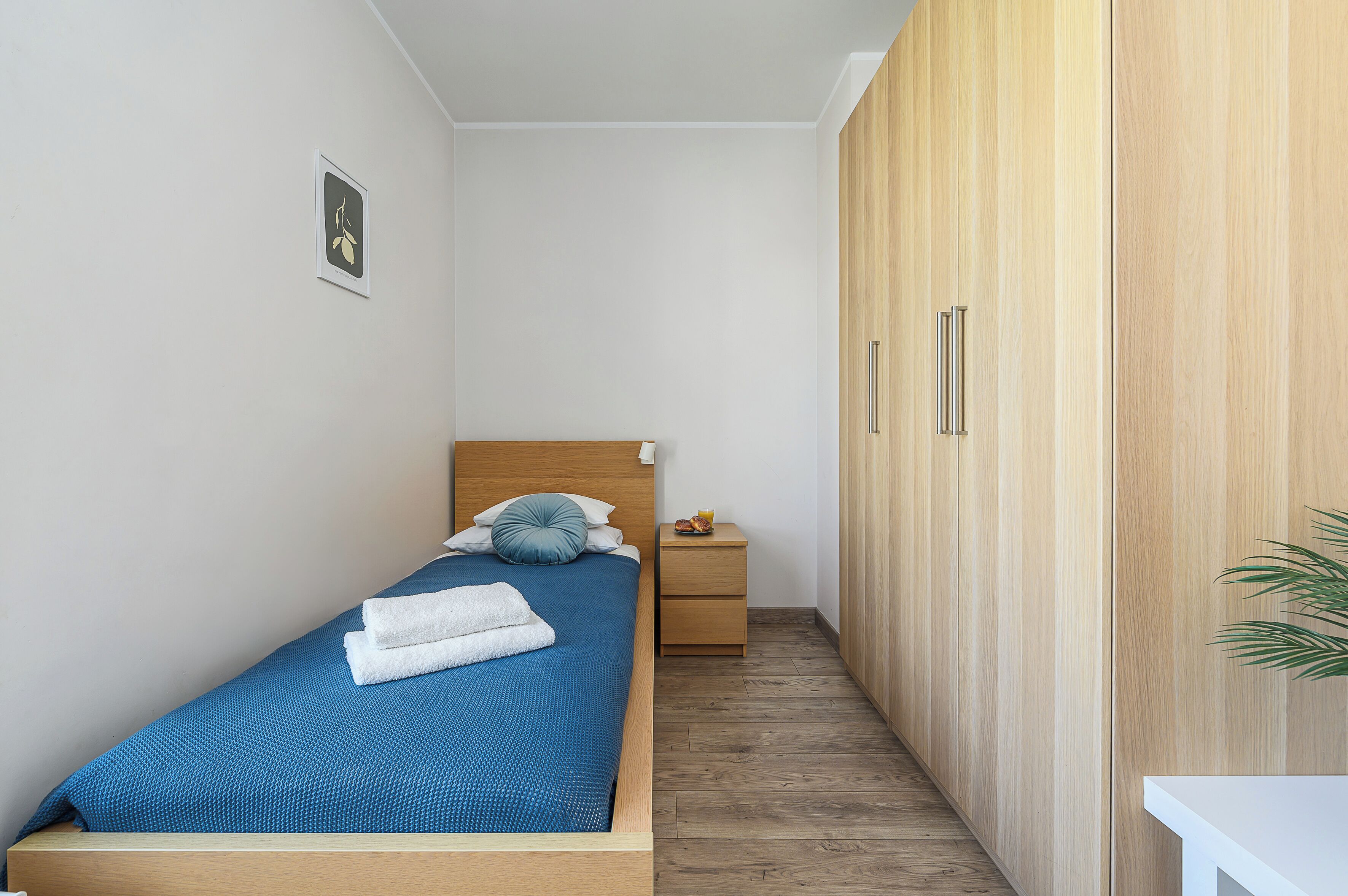 Una camera da letto piccola e ordinata con un letto singolo, un comodino, un armadio e un quadro appeso alla parete.