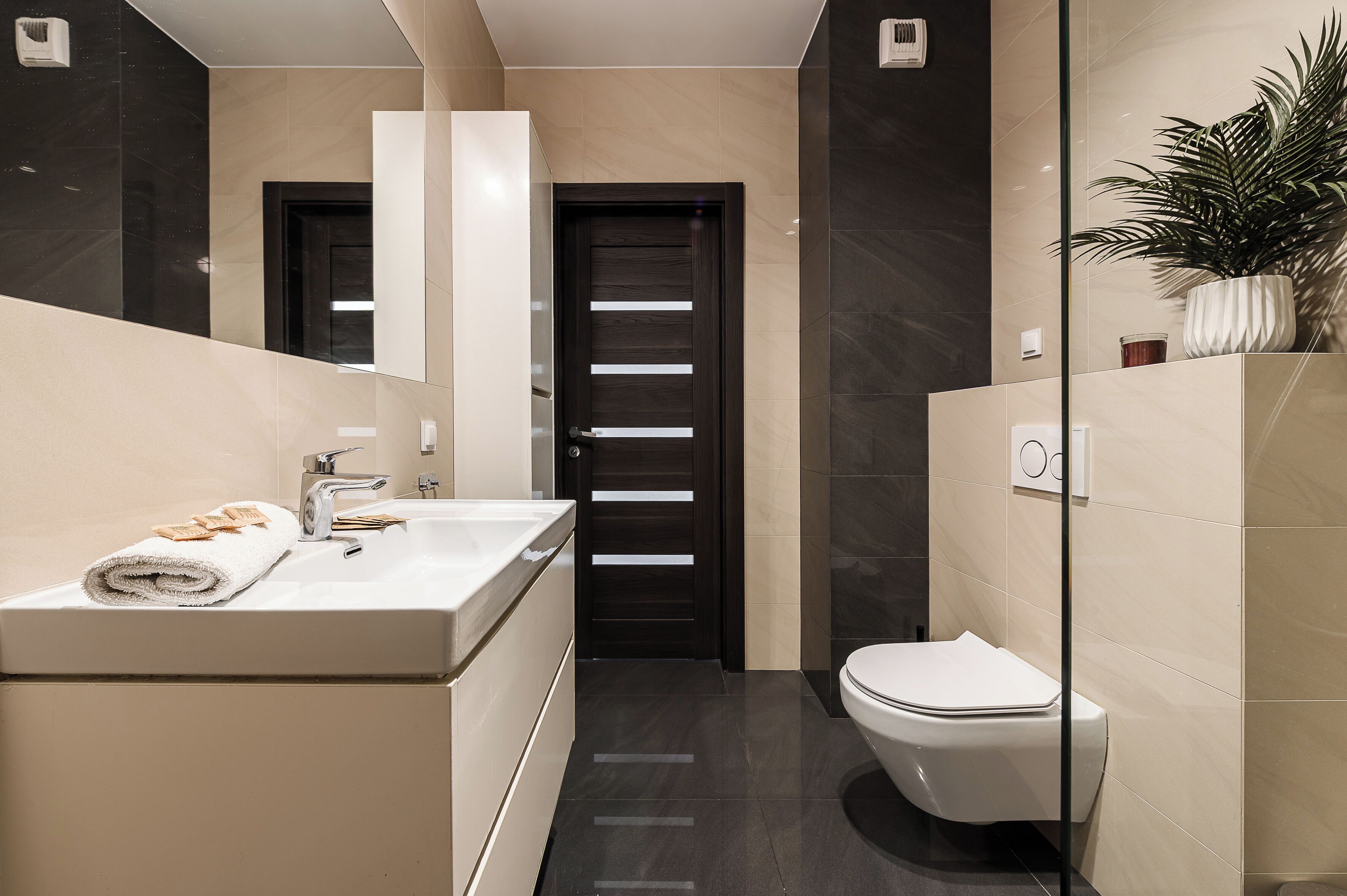 Une salle de bain moderne avec un lavabo blanc, des toilettes et une porte sombre.