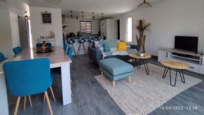 Un salon moderne comprenant un coin repas, un ensemble de canapés, un téléviseur et une cuisine en arrière-plan.