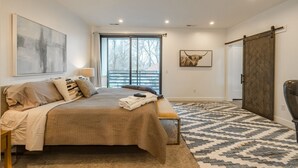 A bedroom with a large bed, a bench, a desk, a chair, a sliding door, and a framed picture on the wall. - Long stays|Desk|Garage (Salt Lake City)