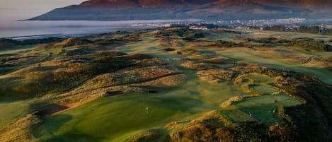 Un campo de golf con colinas onduladas y una cadena montañosa al fondo.