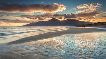 A beach with a mountain in the background, calm waters, and footprints in the sand.