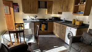 A compact kitchen with wooden cabinets, a microwave, a kettle, and a washing machine. - Cosy Barn Conversion in the Mournes (Newry)