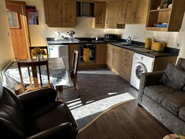 A compact kitchen with wooden cabinets, a microwave, a kettle, and a washing machine.