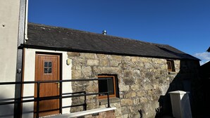 A stone building with a wooden door and window, a metal railing, and a clear blue sky. - Cosy Barn Conversion in the Mournes (Newry)