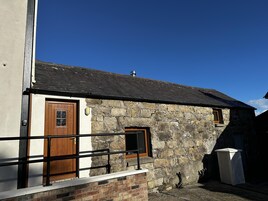 A stone building with a wooden door and window, a metal railing, and a clear blue sky.