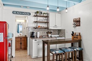 Una cocina con un letrero que dice 'BEACH HOUSE', una mesa de comedor con taburetes y un portal cuchillos de pared.