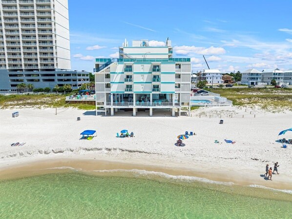 A beachfront hotel with multiple floors, a pool, and beach umbrellas.