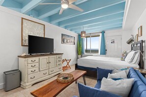 A bedroom with a bed, a television, a dresser, and a window with curtains.