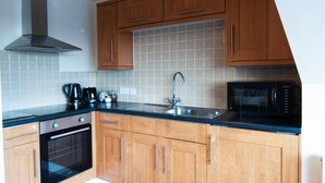 A kitchen with wooden cabinets, a stainless steel range hood, a microwave, a coffee maker, and a built-in oven. - Caribou Suite-Bright & Spacious 2-Bed | Gated Parking | Close to City & Hospital (Burton upon Trent)