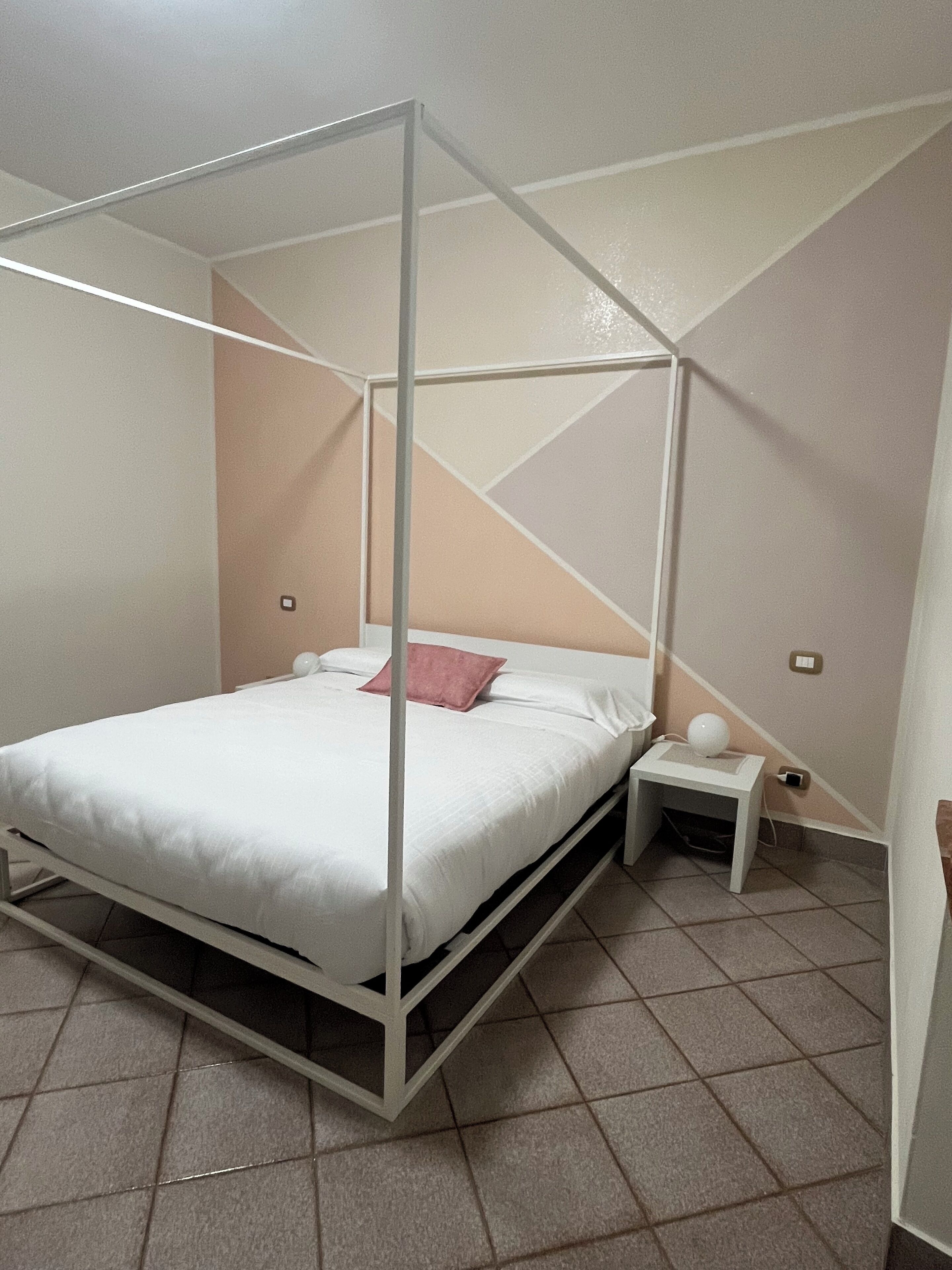A four-poster bed with a white canopy, a small bedside table, and a nightstand with a lamp.