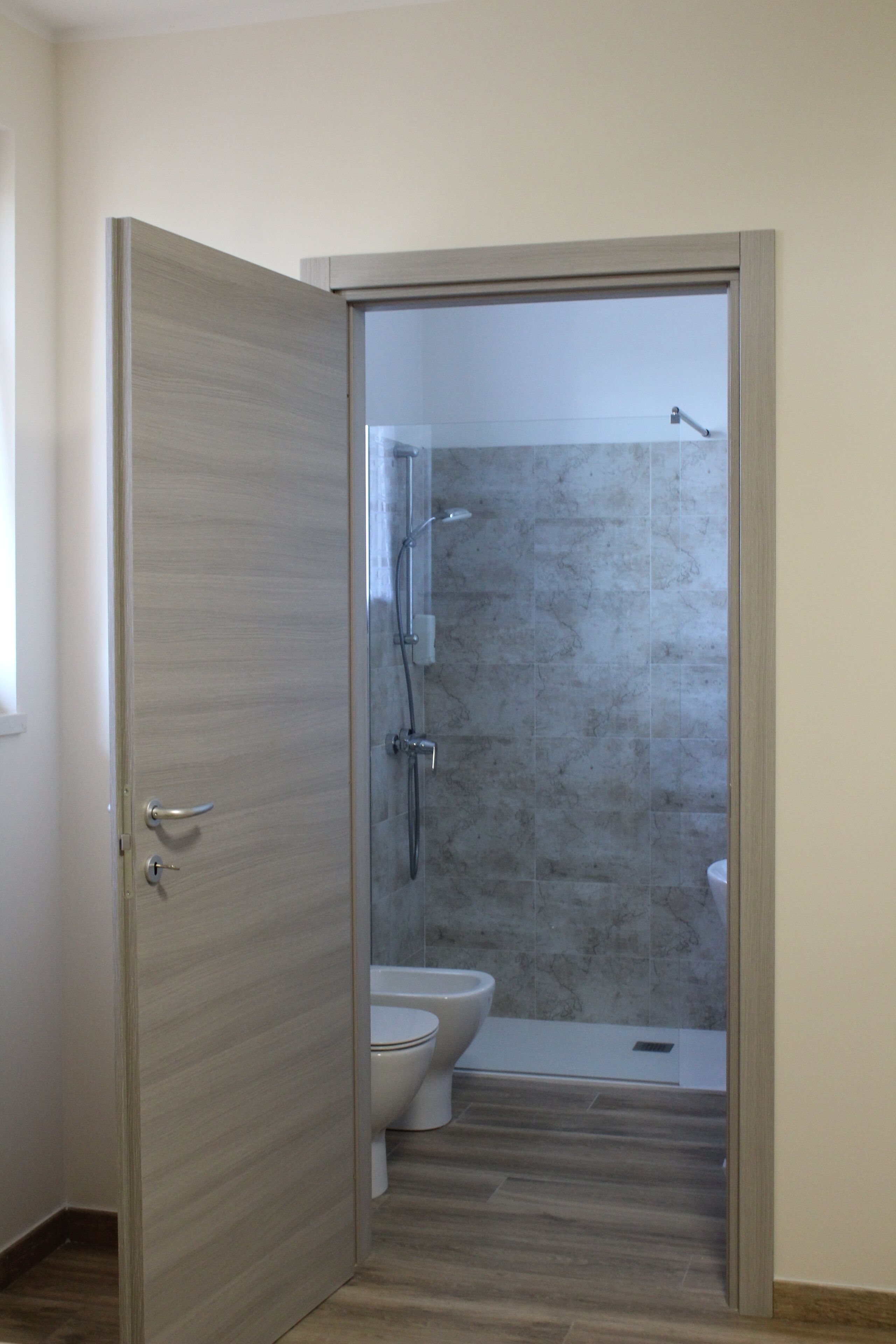 Ein Badezimmer mit Dusche, Toilette und einer Holztür.