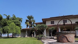 A two-story house with a tiled roof, a stone fountain, and a well-maintained lawn. - B&B VILLA VERONA BIKE (Buttapietra)
