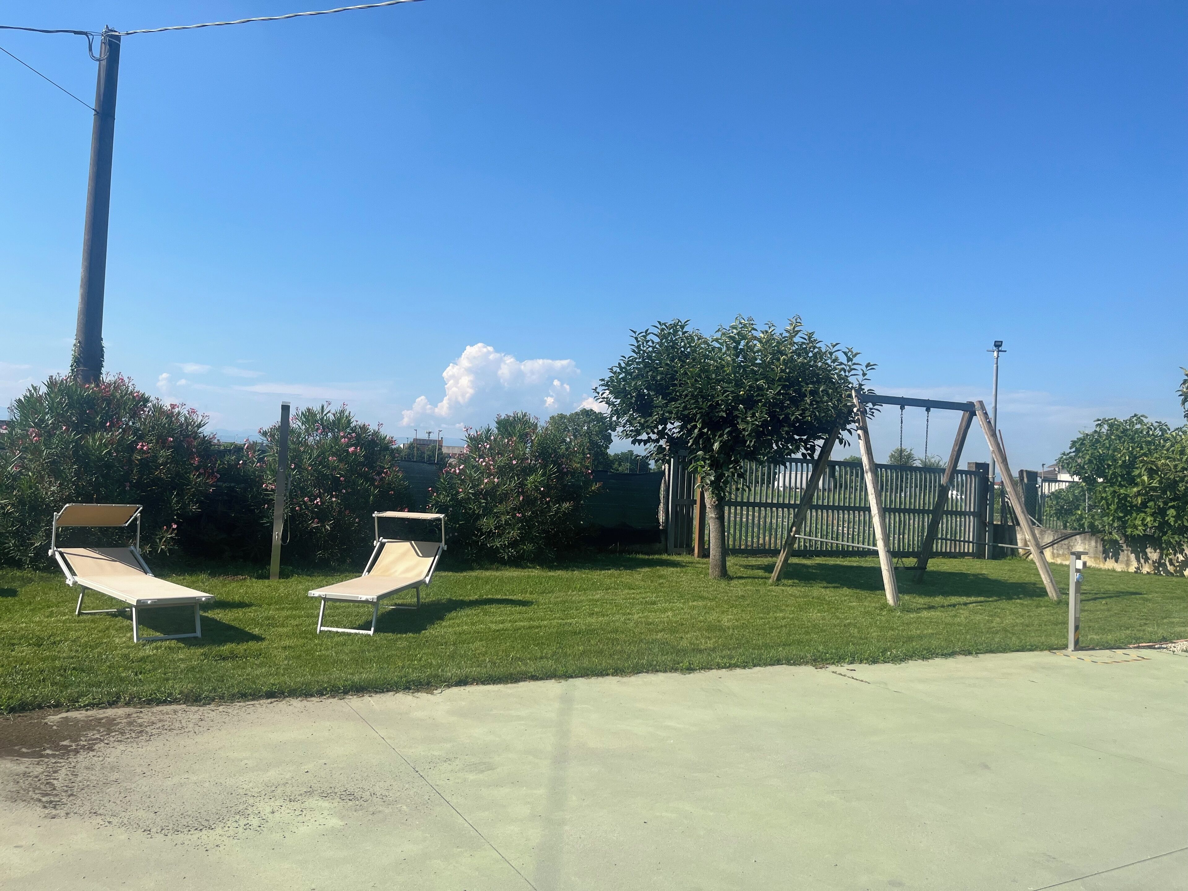 An outdoor area with two sun loungers, a swing set, and a green lawn.