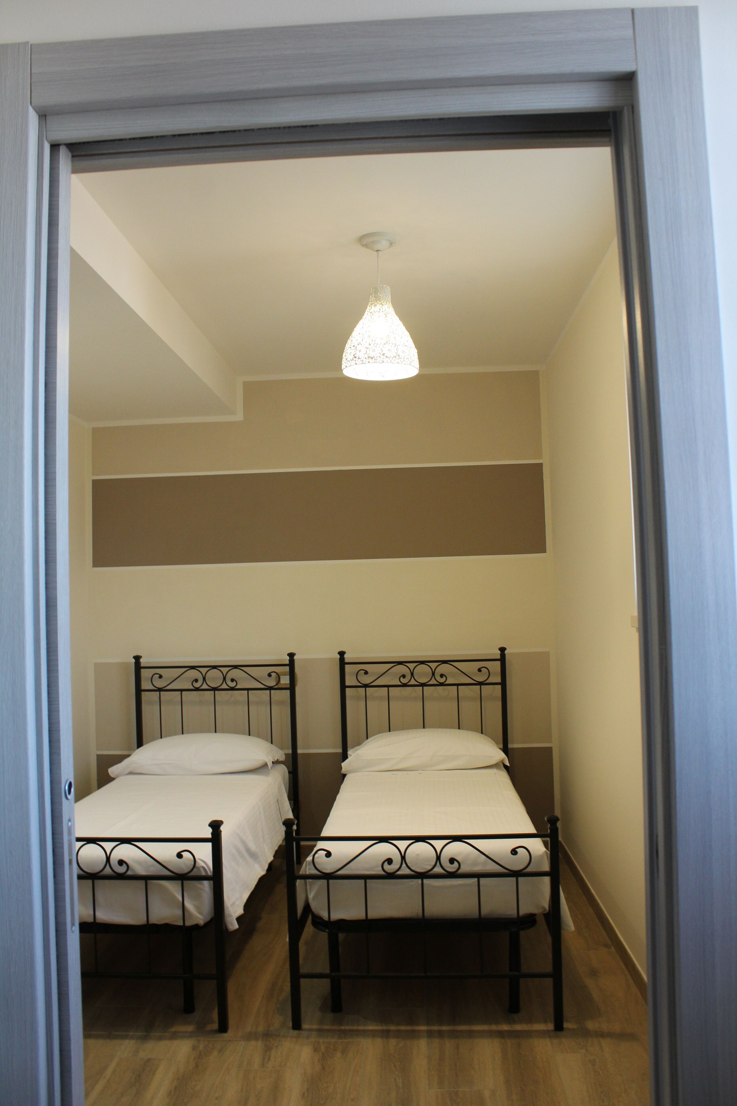 A room with two beds, a hanging light fixture, and a wooden floor.